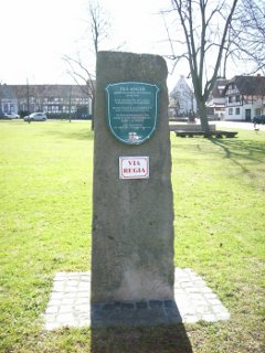 VIA REGIA - Hinweisschild auf dem Sandsteinblock am Anger in Rasdorf, auf dem bereits ein grünes Wappenschild auf die geschichtliche Bedeutung des Angers als Umspann- und Handelsplatz sowie als Lagerplatz für Wallfahrer an der VIA REGIA hinweist